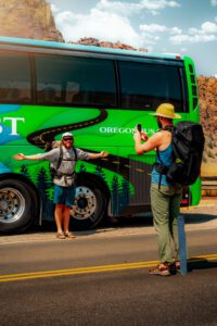 2 people traveling the PCT trail taking a picture on the side of a Pacific Crest Bus Lines charter bus